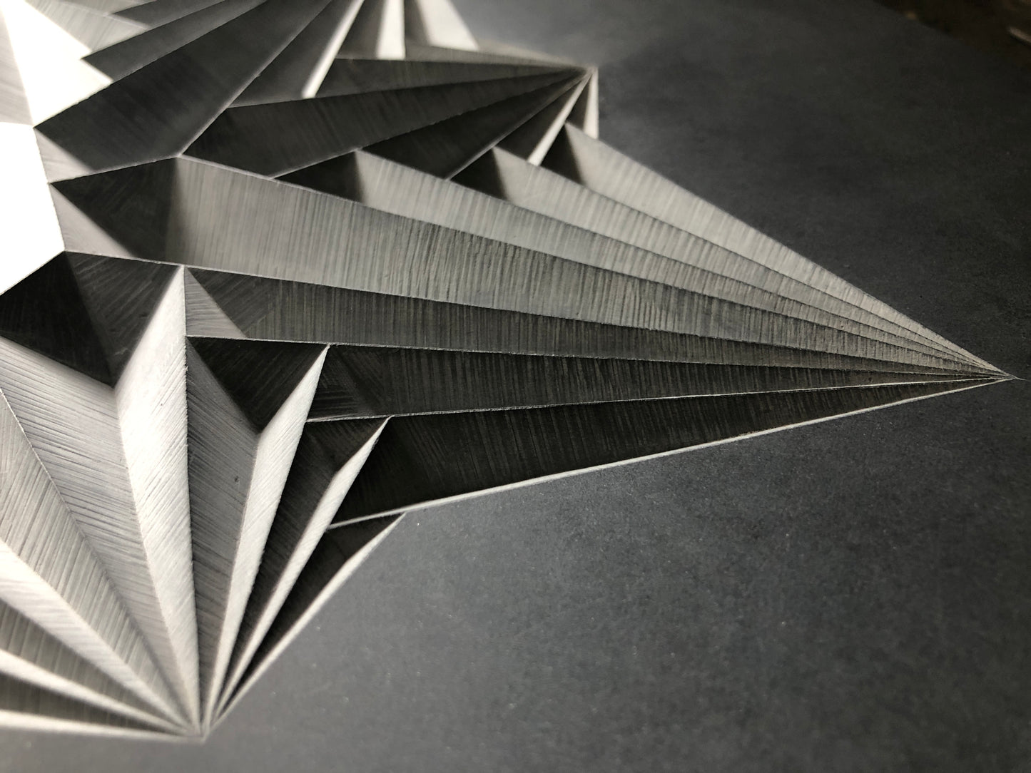 Close-up of "Peace," a paper sculpture by Zoë Wilson Sculpture, showcasing a black and white geometric pattern with sharp, angular folds and intricate textures. Reminiscent of hand-carved Welsh slate, the design offers a modern, abstract appearance with depth and symmetry.