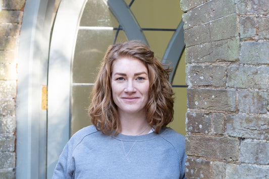 White female with medium length curly red hair casually leaning against a window holding a carved stone sphere
