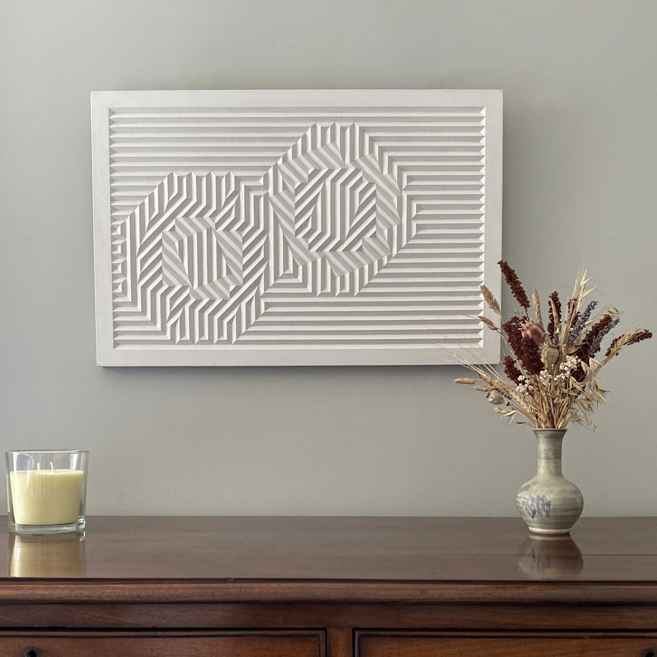 Light coloured cast of a geometric carving hanging on the wall above a chest of drawers