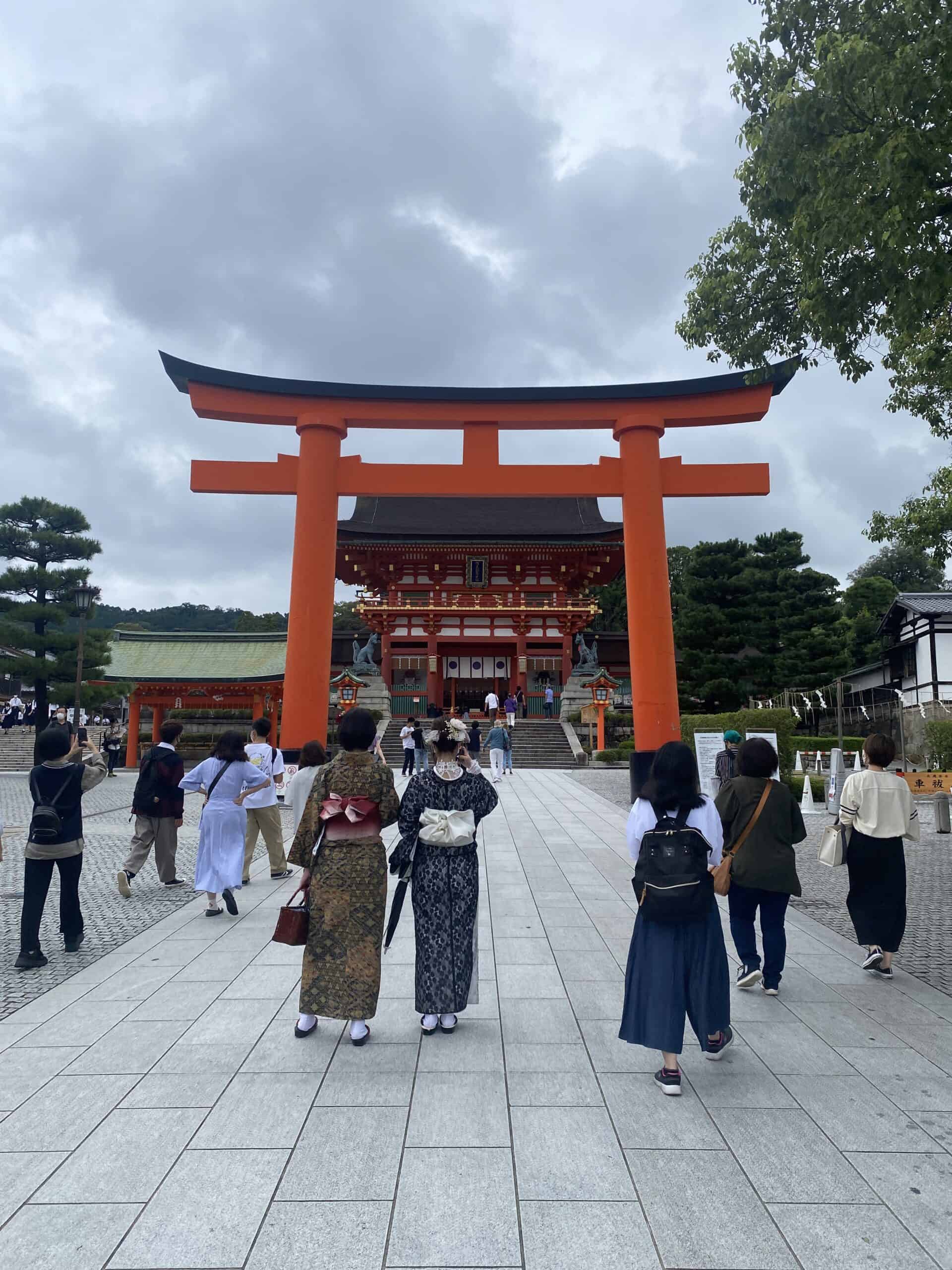 one of the larger red arches at a temple with people stonading in front wearing kimonos