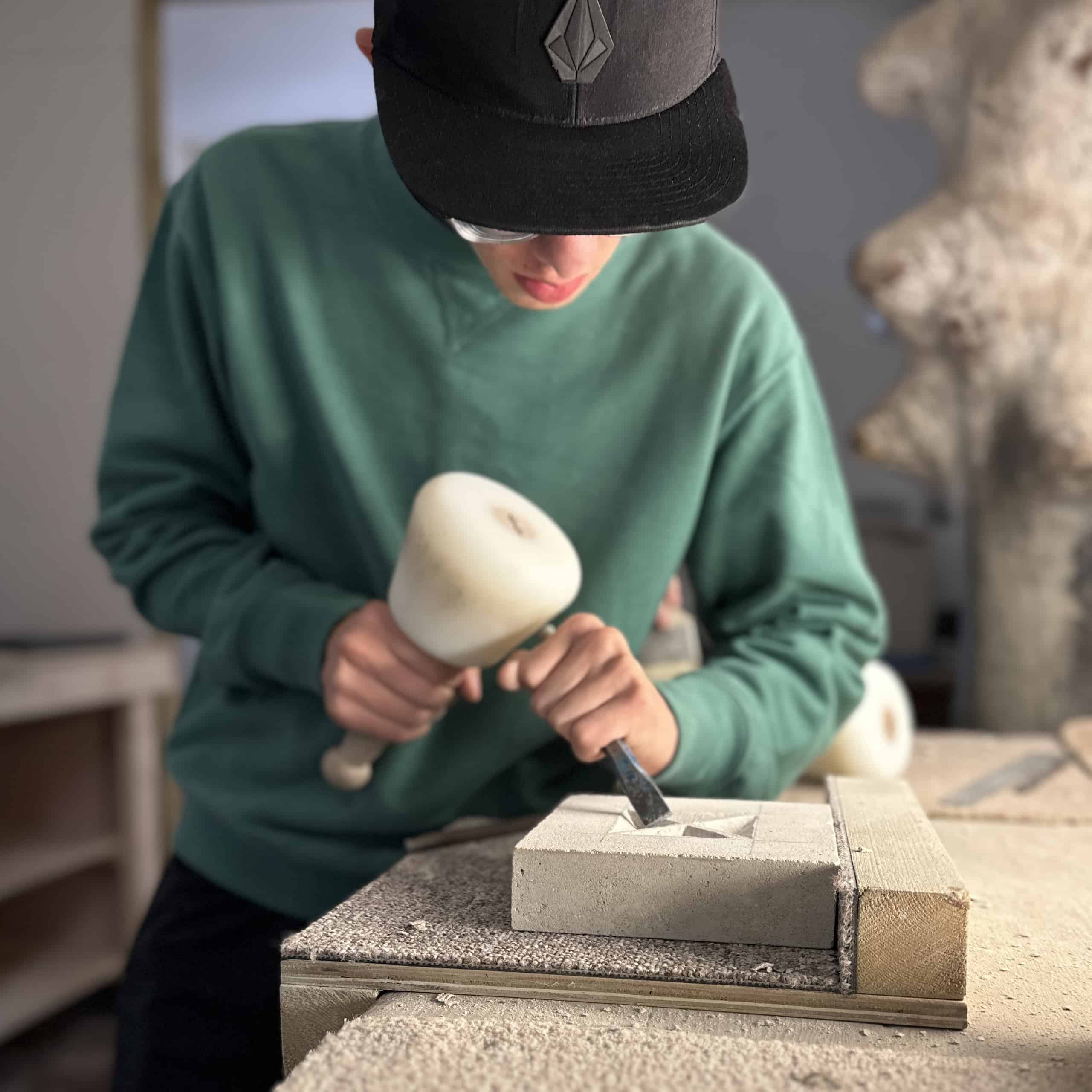 One of Zoë's student learning to carving in her studio holding a mallet and chiselled concentrating on the work infant of them 