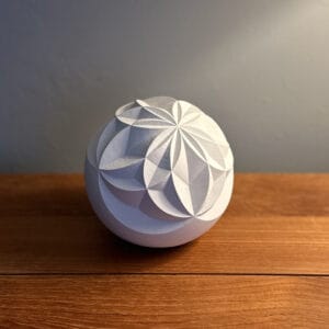 White cast sphere sitting on a wooden table in front of a plain wall