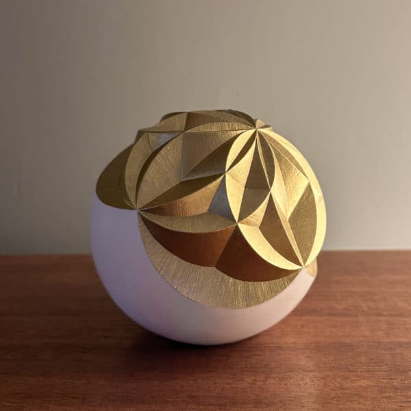 geometric pattern carved into a sphere and painted gold. Sitting on a table next to a light