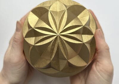 geometric pattern carved into a sphere and painted gold. Being held in hands