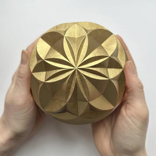 geometric pattern carved into a sphere and painted gold. Being held in hands