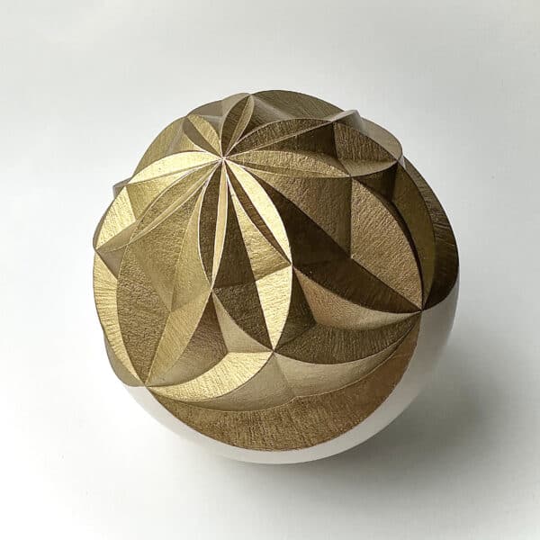 geometric pattern carved into a sphere and painted gold. On a white background